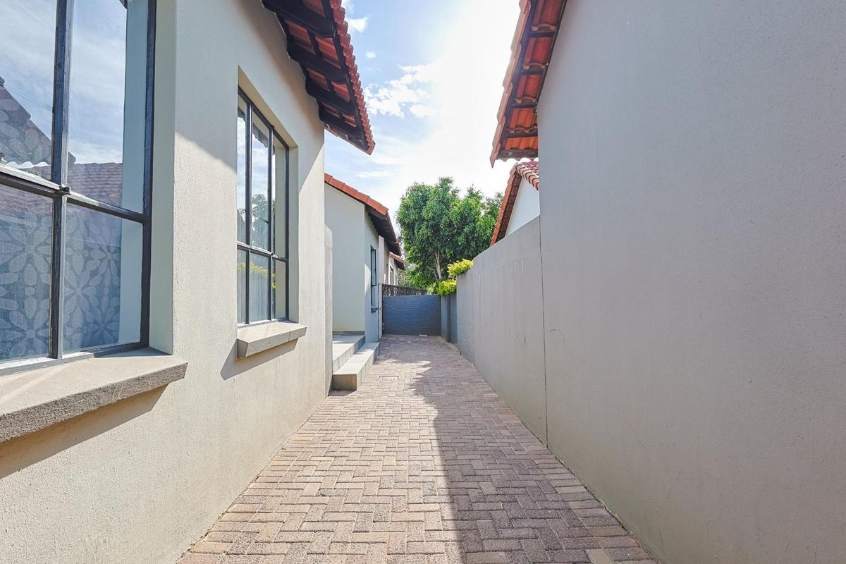A paved side walkway between the main house structure and a boundary wall, featuring tiled roof eaves and exterior lighting.