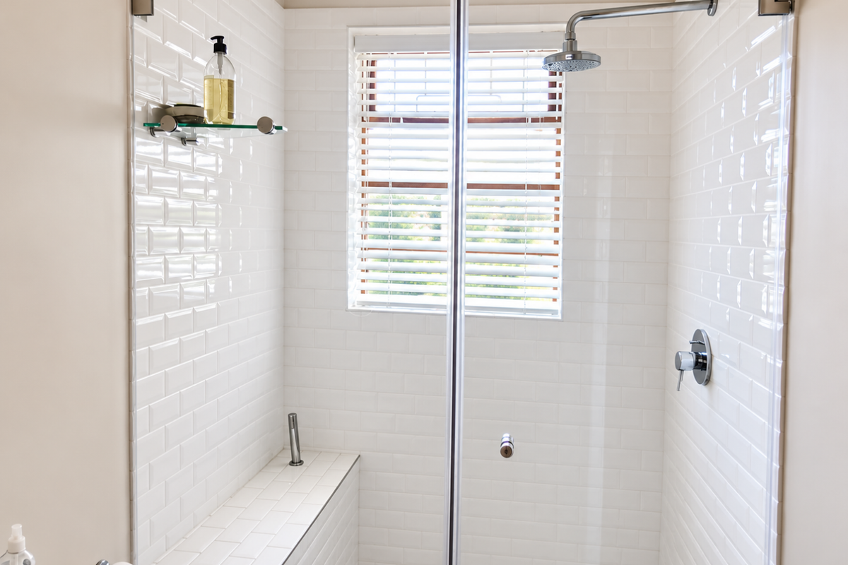 A clean, modern walk-in shower featuring white subway tile walls, a built-in tiled bench, a rain shower head, and a glass enclosure.