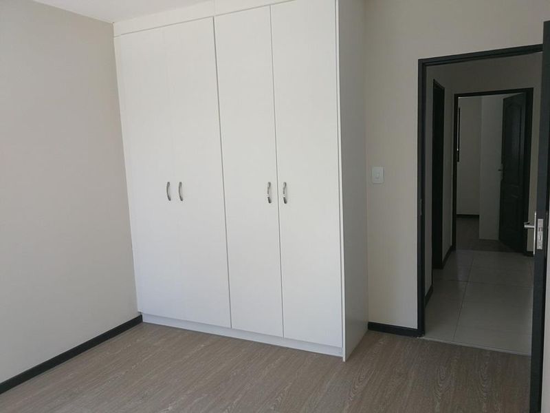 A clean, empty bedroom featuring modern white built-in cupboards, light wood-look laminate flooring, and neutral wall tones, providing a versatile space.