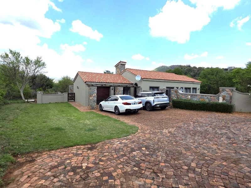 Front elevation of a single-story residence featuring terracotta roof tiles, stone facade accents, and a spacious cobblestone driveway.