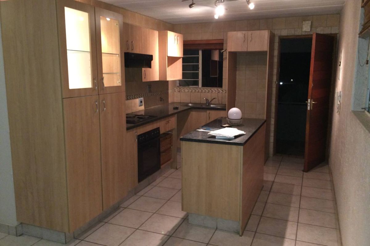 A functional kitchen featuring light wood cabinetry, dark laminate countertops, a central island, and tiled flooring with integrated appliances.