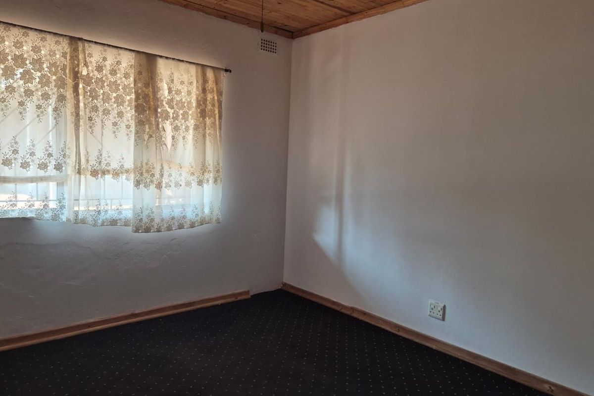 An empty bedroom featuring a timber-clad ceiling, dark carpeting, and a window with natural light, offering a blank canvas for renovation.