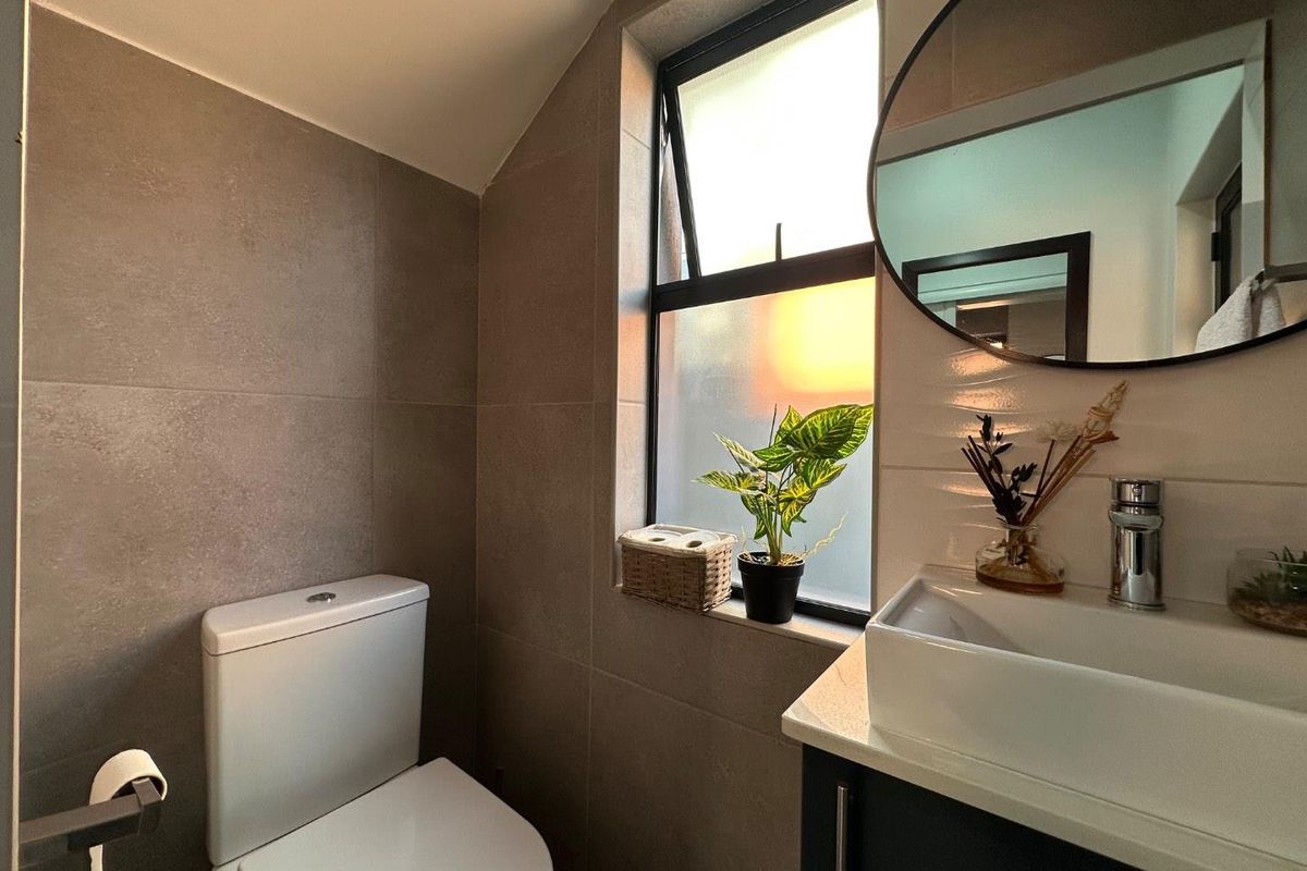 A modern, compact bathroom featuring neutral wall tiling, a sleek vanity with a vessel sink, and a window providing natural light.