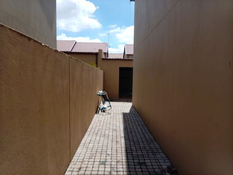 A narrow paved side passage between two boundary walls leading to the rear of the townhouse property.