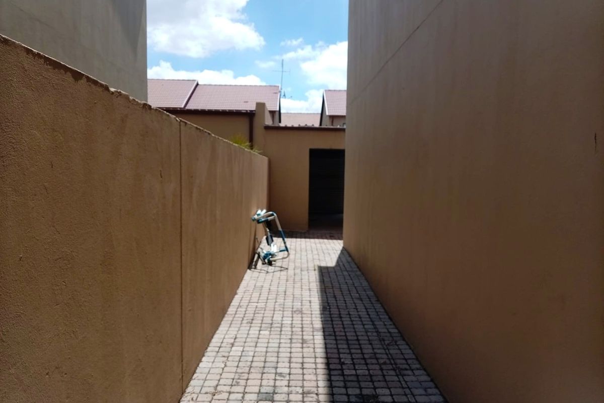 A narrow paved side passage between two boundary walls leading to the rear of the townhouse property.