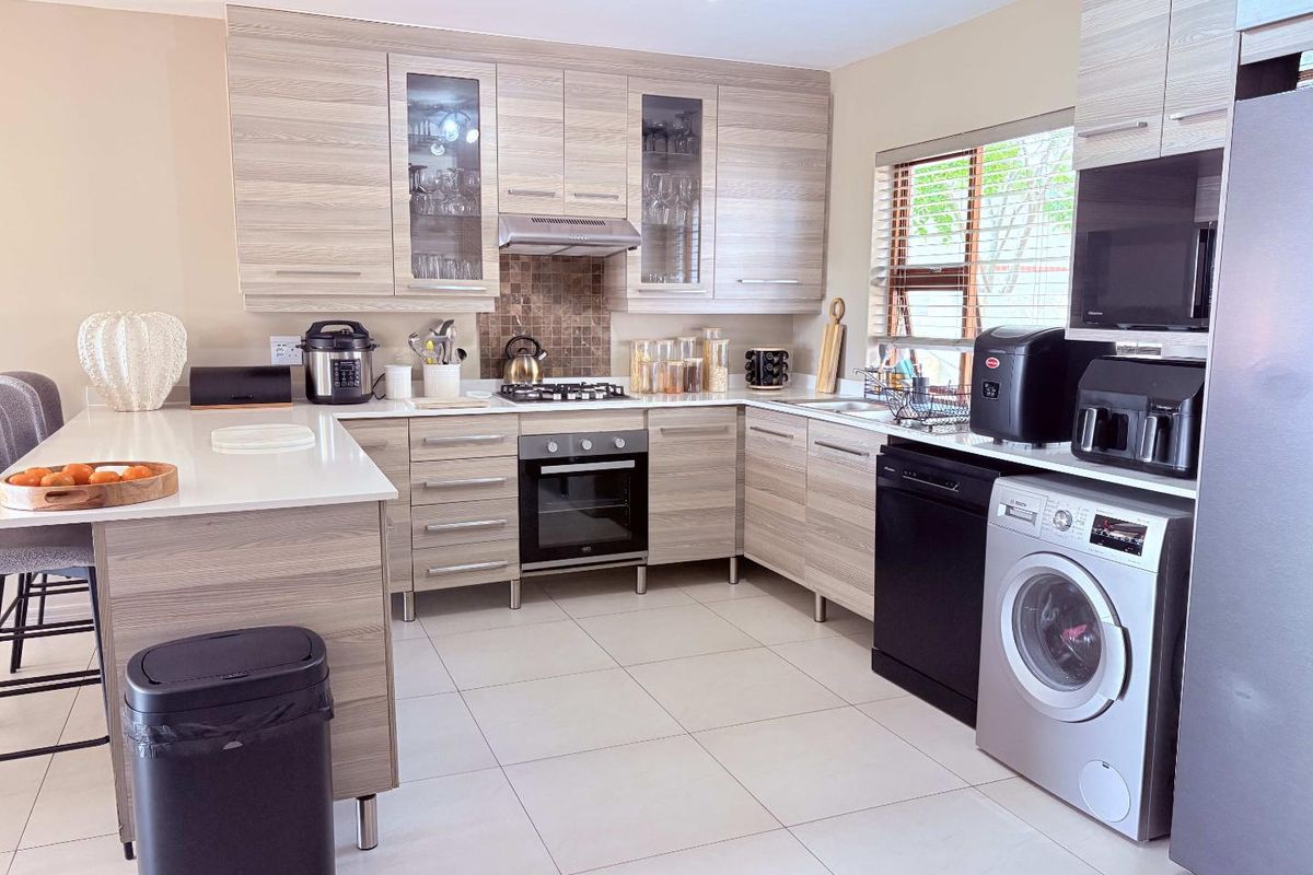 Modern kitchen featuring light wood-grain cabinetry, stone countertops, a central island, built-in oven, gas hob, and integrated laundry plumbing.