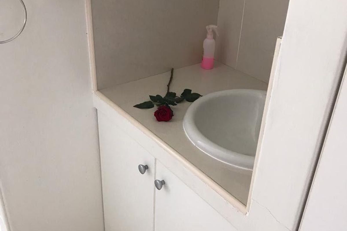 A compact bathroom vanity area featuring a built-in cabinet, drop-in sink, and tiled backsplash, showing signs of wear on the cabinetry.