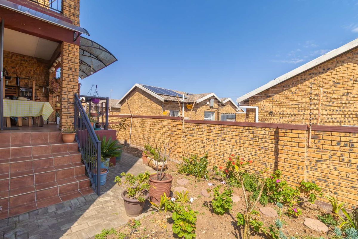 A view of the rear exterior area featuring a brick boundary wall, paved walkway, and a raised patio with tiled steps.