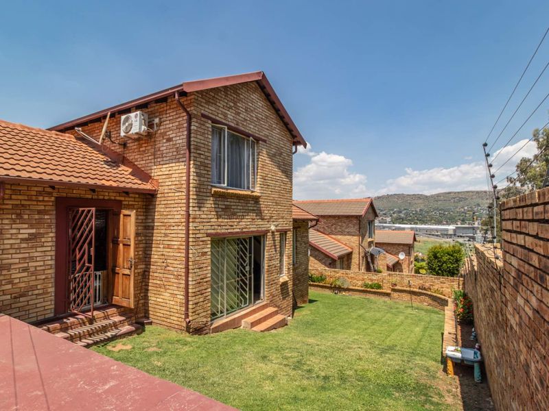 Rear view of a face brick townhouse featuring a private lawn, perimeter wall with electric fencing, and sliding door access.