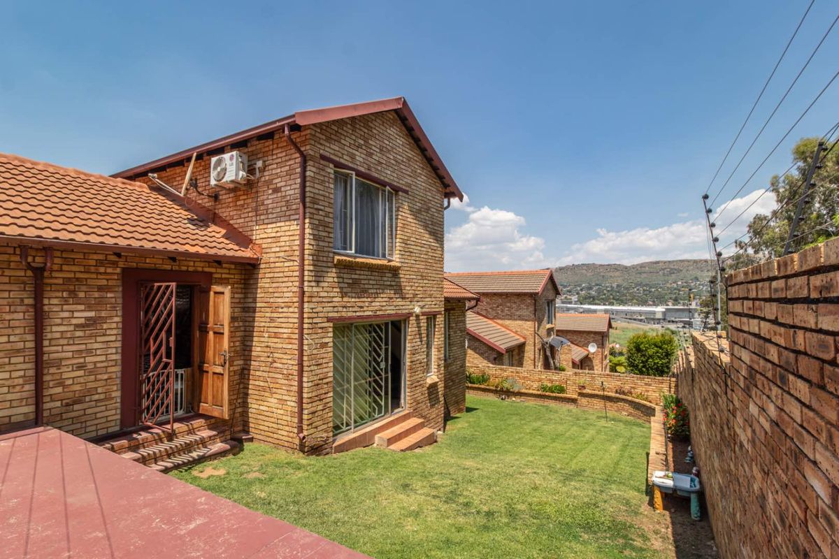 Rear view of a face brick townhouse featuring a private lawn, perimeter wall with electric fencing, and sliding door access.