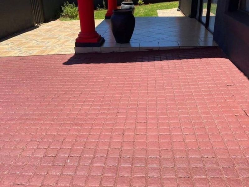 A covered patio area featuring tiled flooring and decorative columns, leading out to a paved outdoor space and enclosed garden.