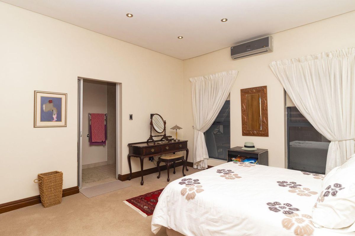 A spacious bedroom featuring neutral carpeting, recessed ceiling lighting, and a wall-mounted air conditioning unit, with an adjoining en-suite bathroom.