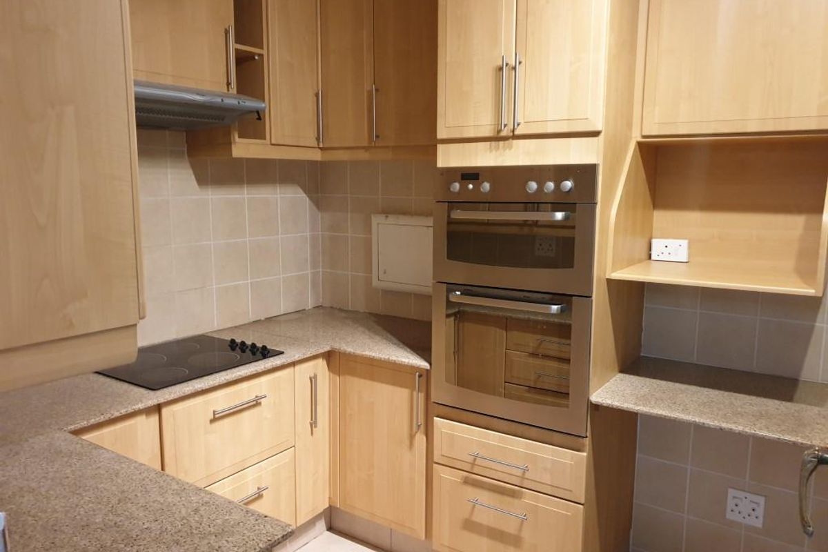 A functional kitchen featuring light wood cabinetry, granite countertops, a built-in double oven, and an electric hob with a tiled splashback.