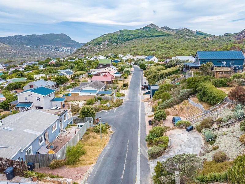 An aerial view of a residential street in a coastal hillside neighborhood, showcasing the surrounding landscape and existing housing development.