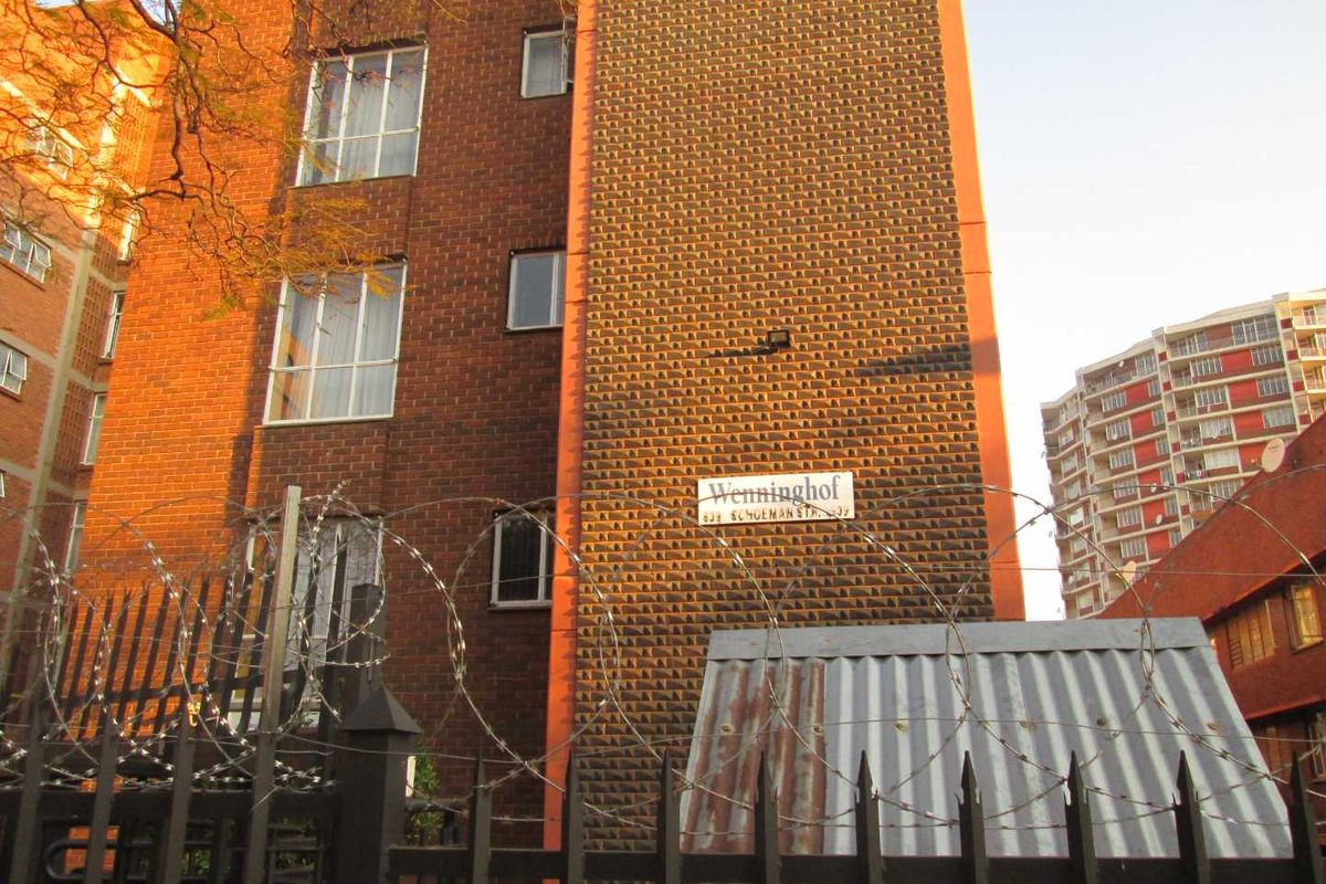 Exterior view of the Wenninghof apartment building, featuring a brick facade, secure perimeter fencing with razor wire, and a metal entrance structure.
