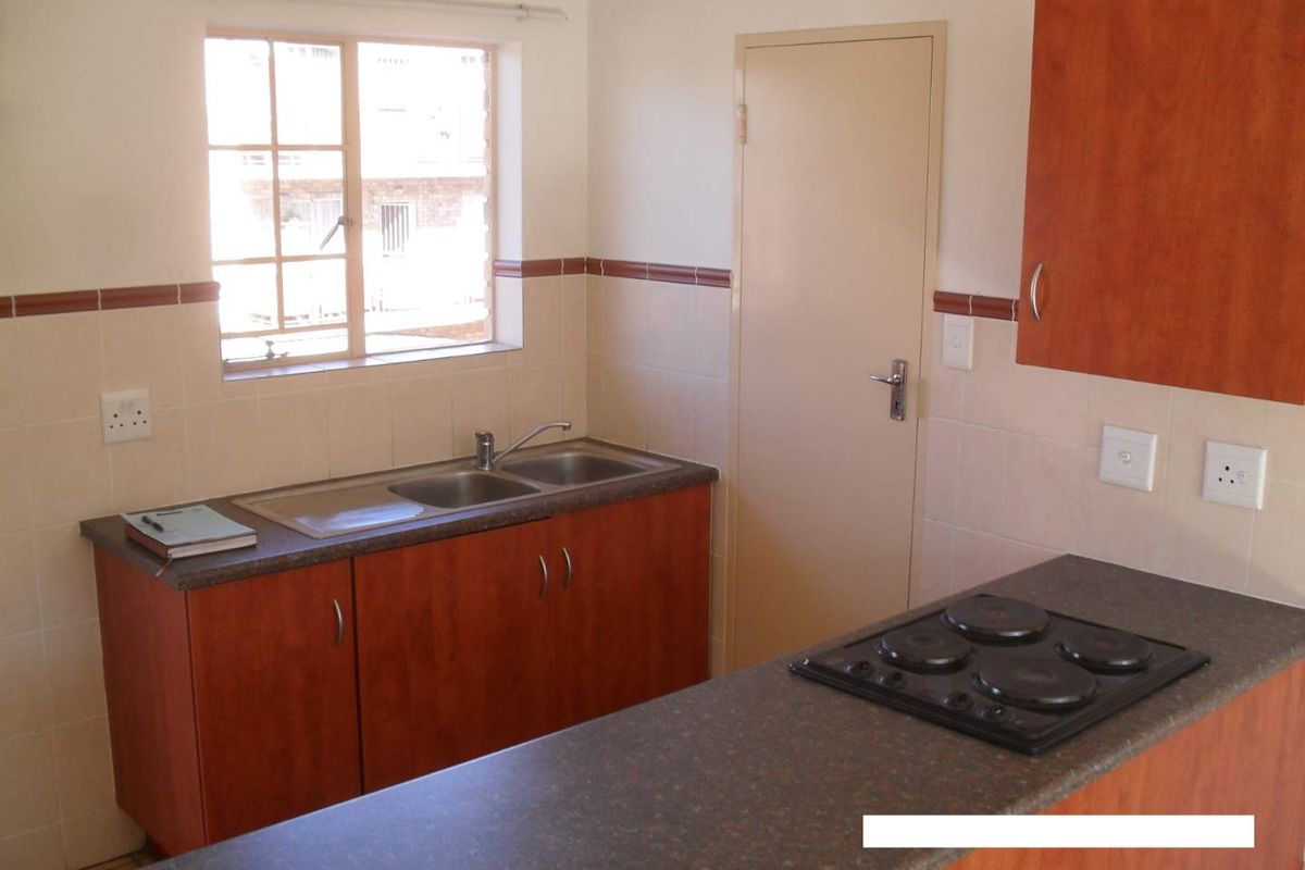 A functional kitchen featuring laminate countertops, built-in cabinetry, a double bowl sink, and an integrated electric hob with tiled splashback.