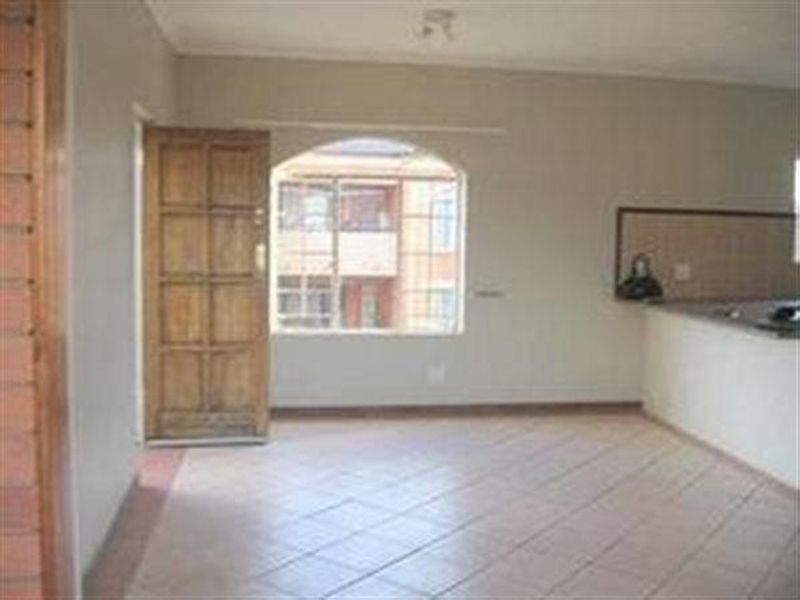 An open-plan living area featuring tiled flooring, a wooden entrance door, and an arched window, with an adjacent kitchen counter area.