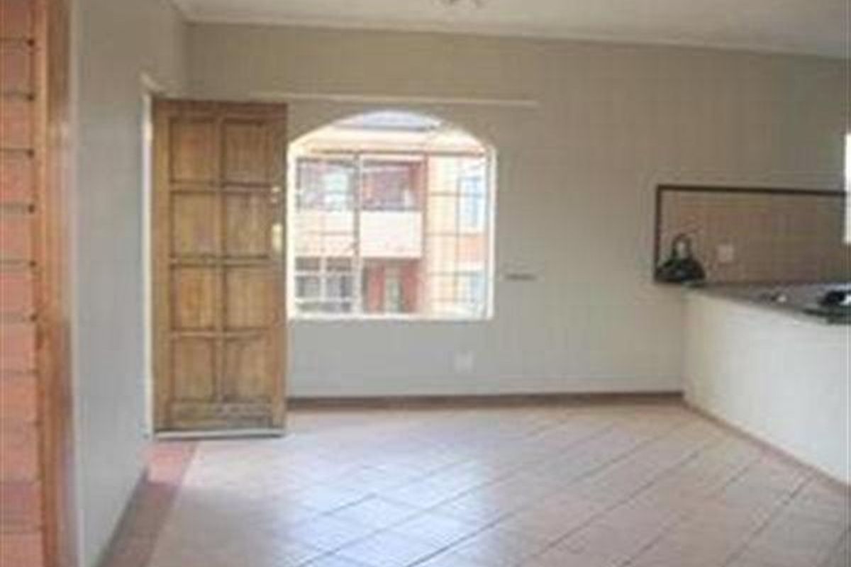 An open-plan living area featuring tiled flooring, a wooden entrance door, and an arched window, with an adjacent kitchen counter area.