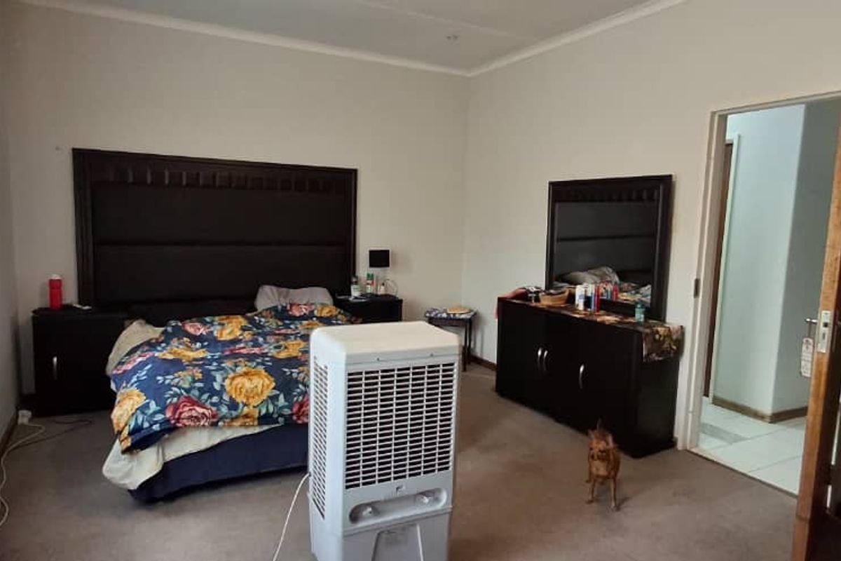 A spacious bedroom featuring neutral wall tones, carpeted flooring, and a doorway leading to an adjacent room.