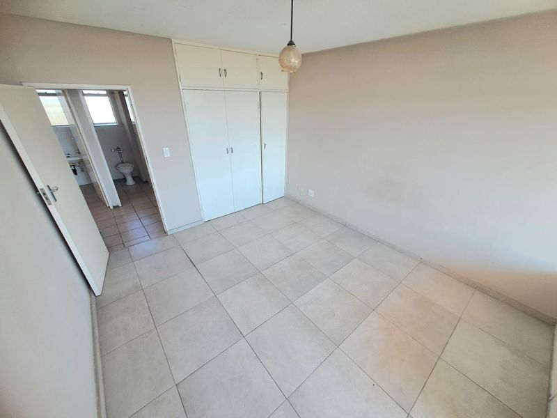 An empty bedroom featuring neutral tiled flooring, built-in cupboards, and an adjacent bathroom entrance.