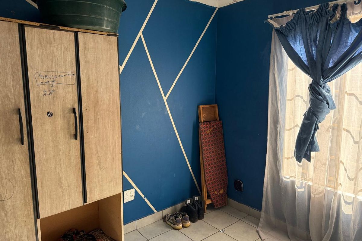 A bedroom featuring tiled flooring and a blue accent wall with geometric detailing, requiring minor cosmetic updates to the paintwork and ceiling finishes.