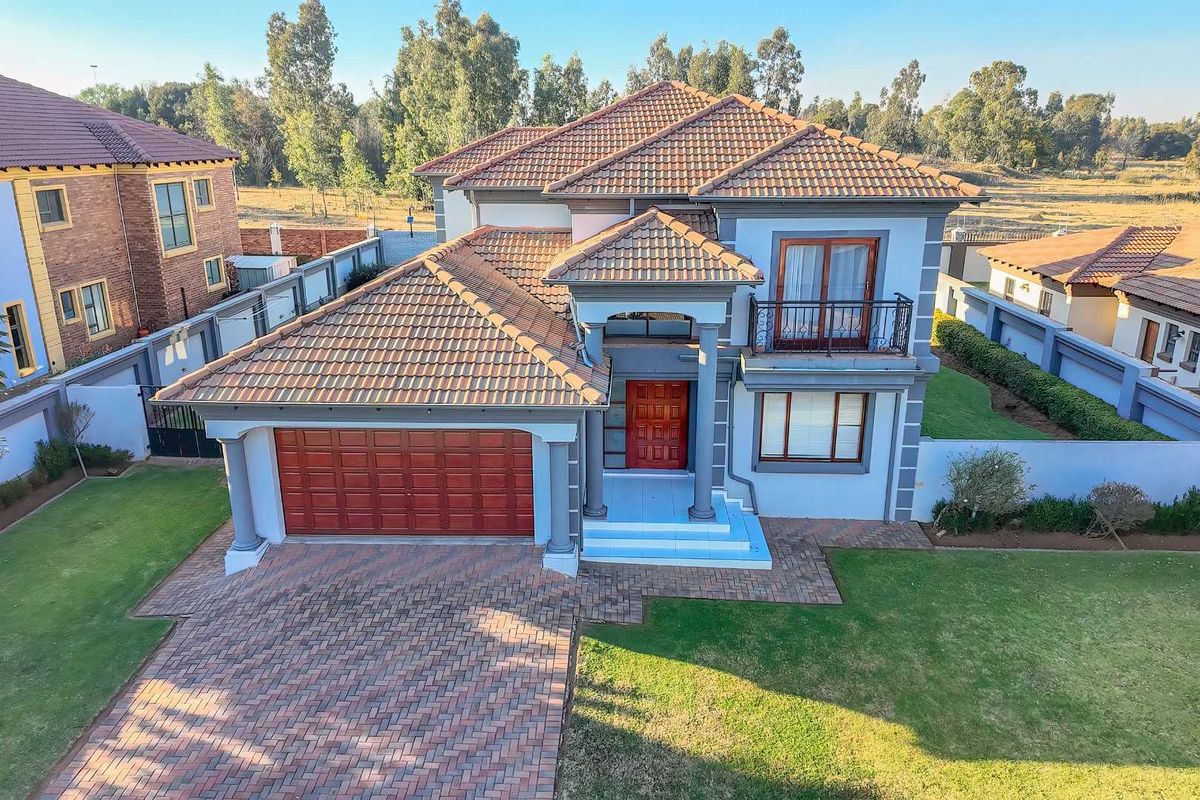 Aerial view of a double-story residential property featuring a tiled roof, paved driveway, double garage, and a balcony with wrought iron railings.