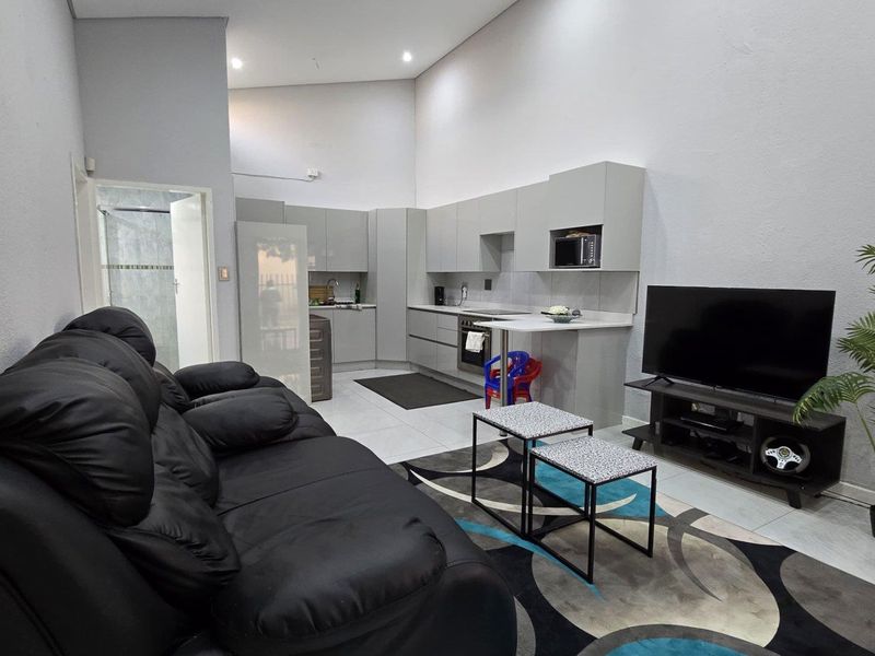 Modern open-plan living area featuring a sleek kitchen with built-in appliances, high ceilings, and tiled flooring, creating a bright and functional space.