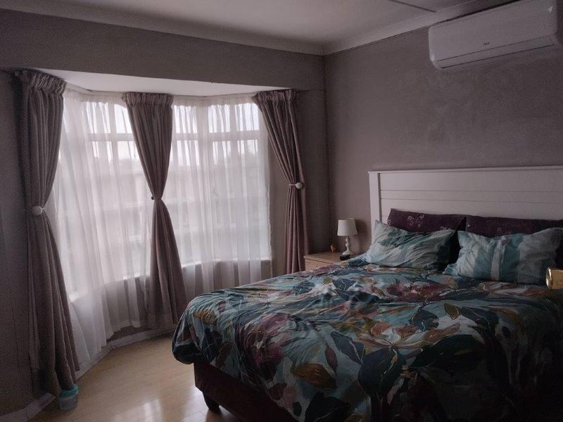 A bedroom featuring a bay window, laminate flooring, and a wall-mounted split-system air conditioner.