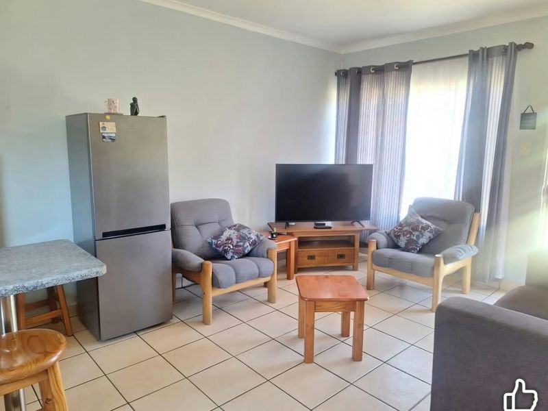 A functional living area featuring neutral tiled flooring and large windows with curtain tracks, providing a bright and practical space.