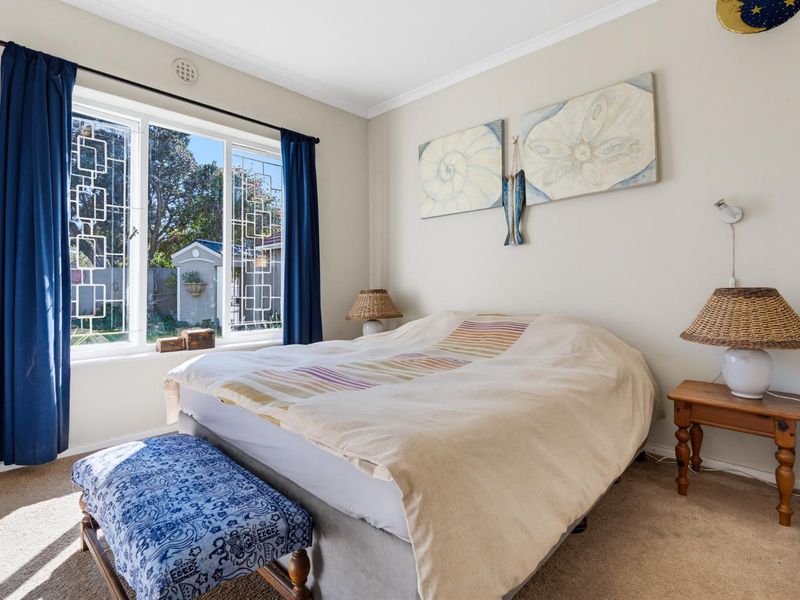 A well-lit bedroom featuring neutral walls, wall-to-wall carpeting, and large windows with decorative security grilles overlooking the garden.