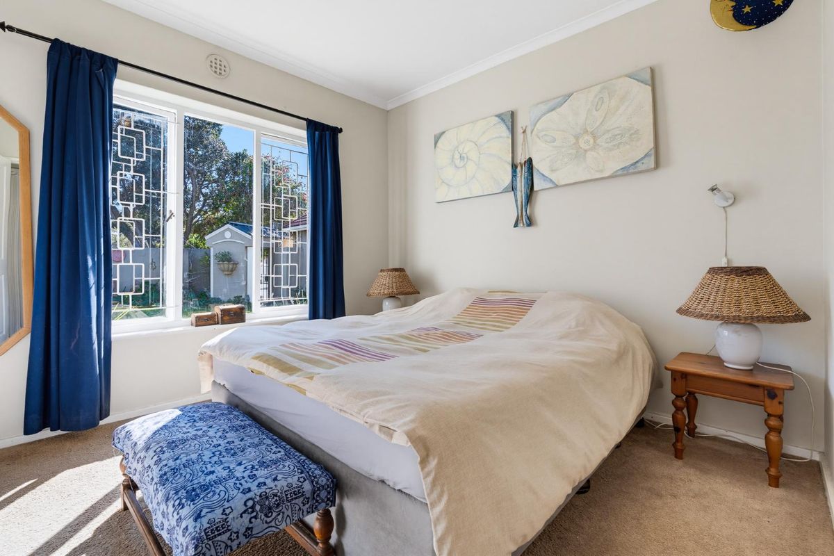 A well-lit bedroom featuring neutral walls, wall-to-wall carpeting, and large windows with decorative security grilles overlooking the garden.