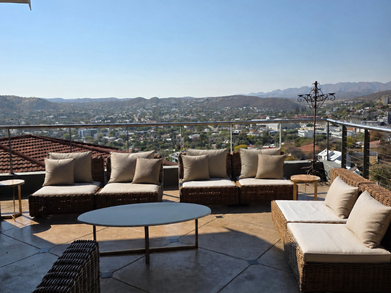 Spacious outdoor balcony featuring a glass balustrade and tiled flooring, offering expansive panoramic views of the surrounding city and mountain landscape.
