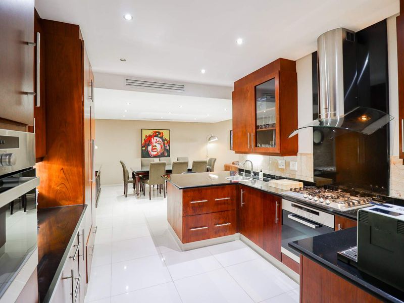 Modern open-plan kitchen featuring rich wood cabinetry, granite countertops, integrated appliances, and recessed lighting, flowing seamlessly into the adjacent dining area.