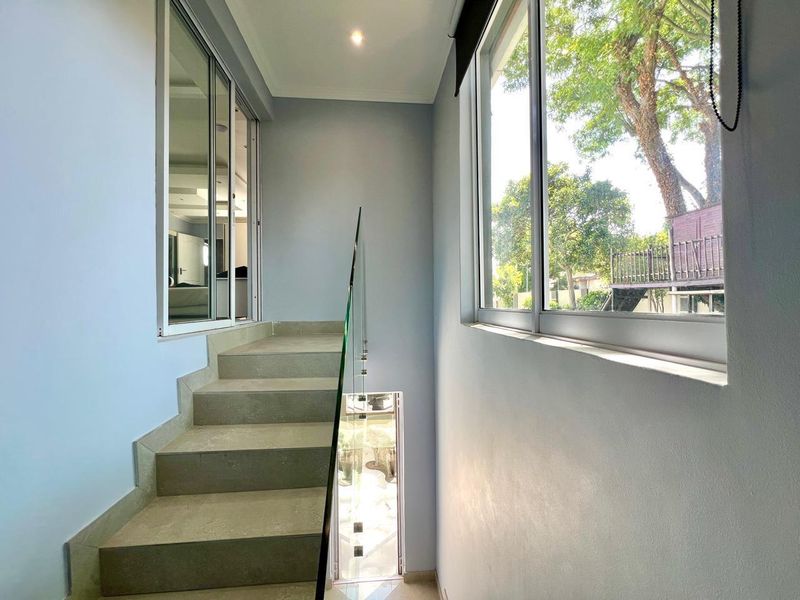 A bright, modern staircase landing featuring a sleek glass balustrade, tiled steps, and large windows providing ample natural light.