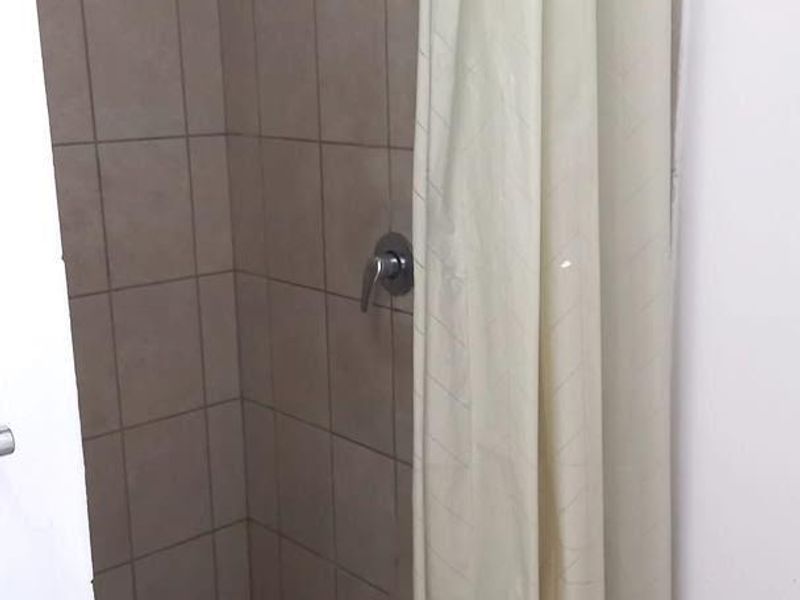 A functional shower stall featuring tiled walls and flooring, equipped with a standard shower head and mixer tap.