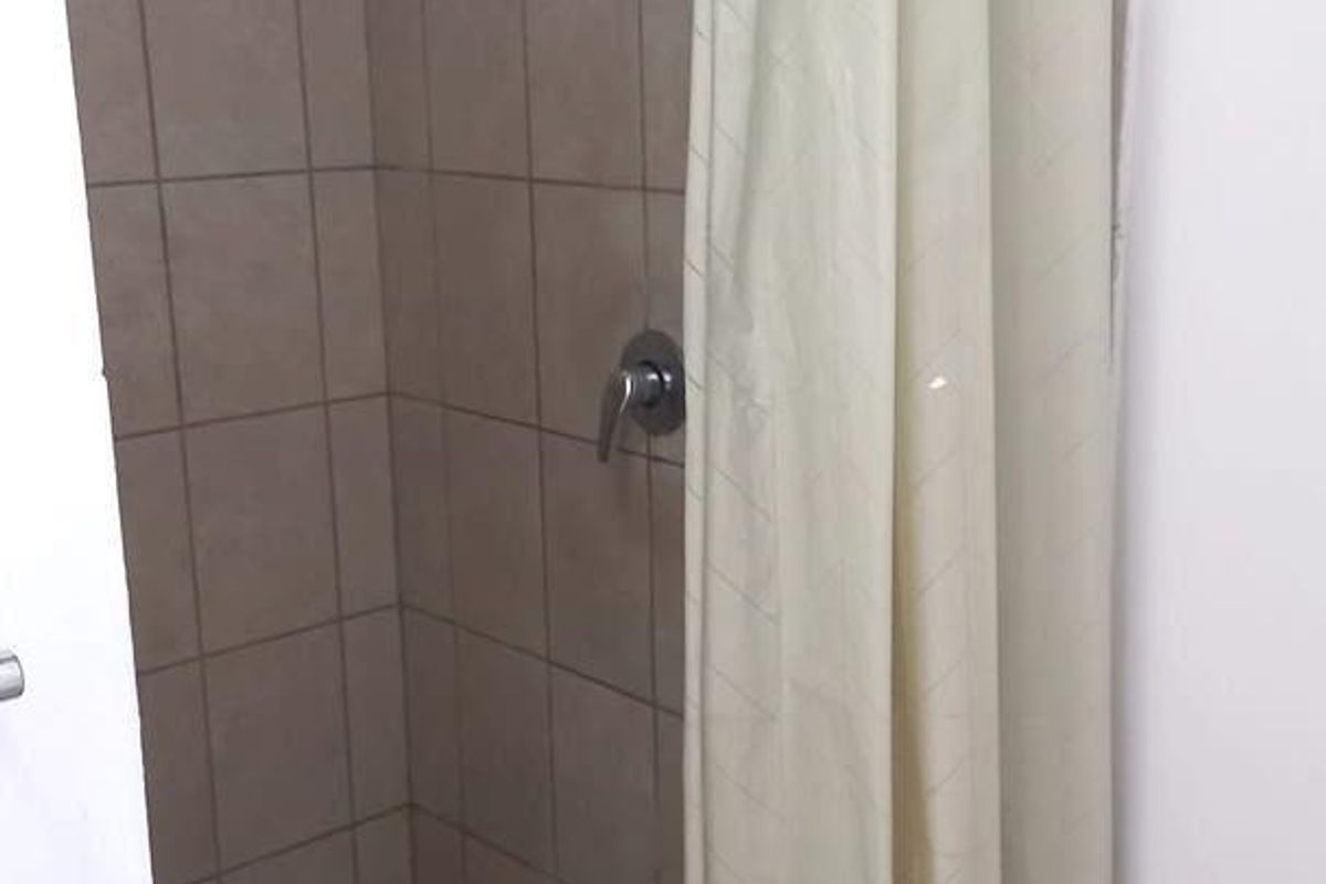 A functional shower stall featuring tiled walls and flooring, equipped with a standard shower head and mixer tap.
