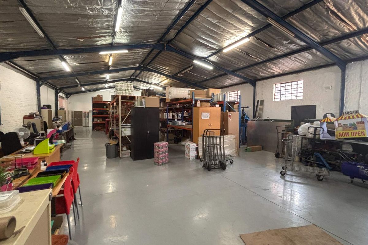 Spacious industrial utility or warehouse area featuring exposed steel roof trusses, durable concrete flooring, and functional fluorescent lighting, suitable for storage or workshop use.