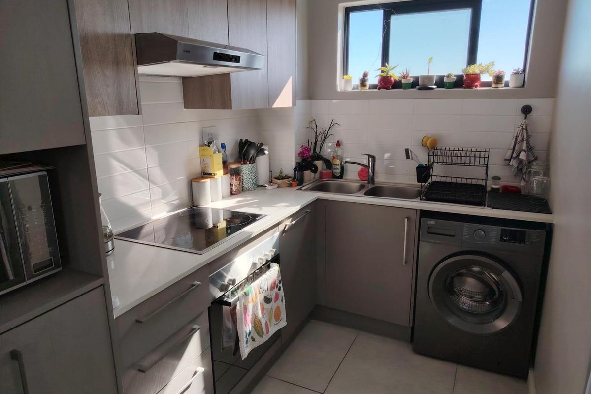 Modern compact kitchen featuring sleek cabinetry, integrated appliances, electric hob, extractor fan, and a double sink with tiled flooring.