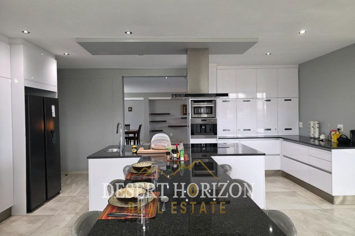 Modern kitchen featuring high-gloss white cabinetry, black granite countertops, a central island with breakfast bar, and integrated stainless steel appliances.