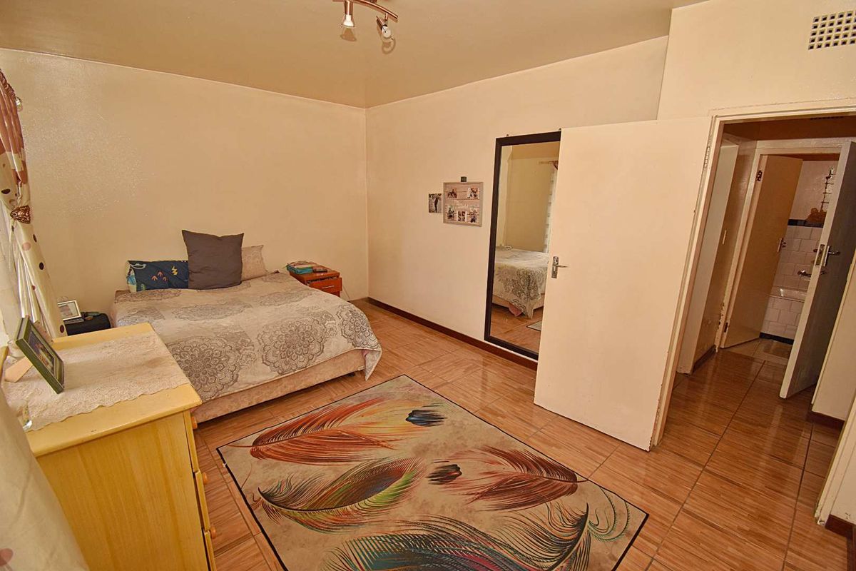 A bedroom featuring tiled flooring, a built-in mirror, and direct access to an adjacent bathroom.