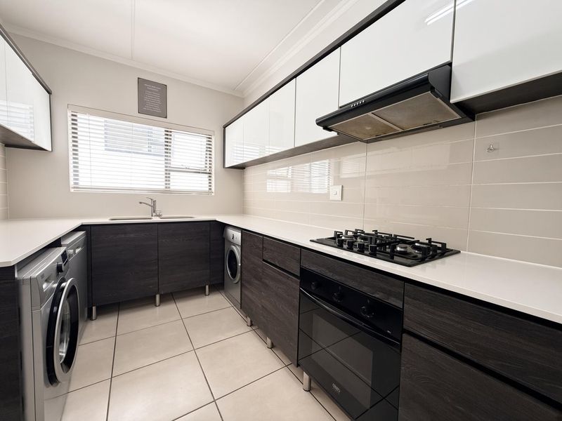 Modern kitchen featuring dark wood cabinetry, white countertops, gas hob, built-in oven, extractor fan, and integrated laundry space with tiled flooring.