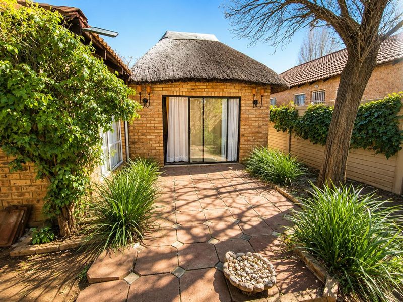A private rear courtyard featuring a paved patio area, established garden, and a structure with a traditional thatched roof and sliding glass door access.