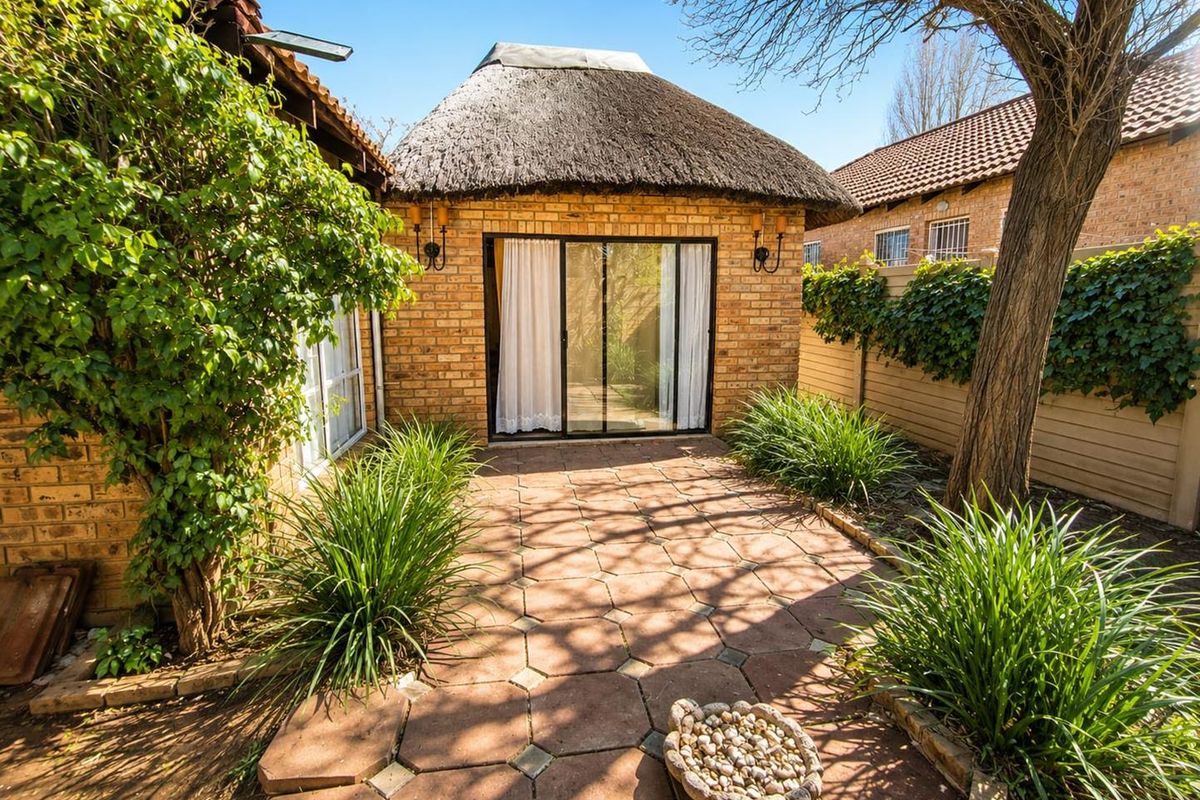 A private rear courtyard featuring a paved patio area, established garden, and a structure with a traditional thatched roof and sliding glass door access.