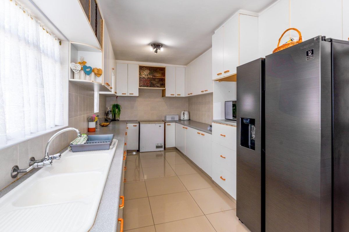 A functional kitchen featuring white cabinetry, tiled flooring, a double basin sink, and ample counter space for meal preparation.