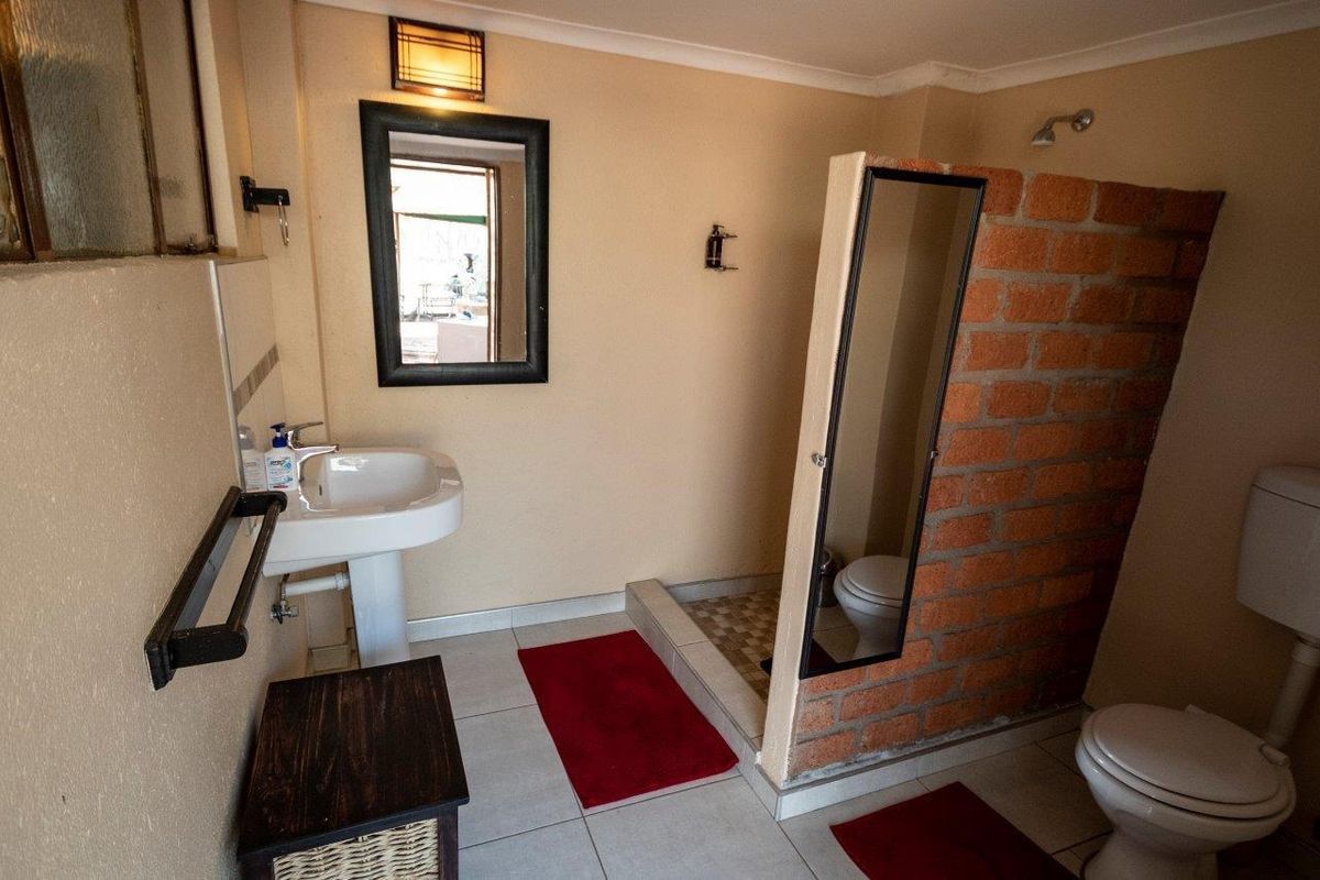 A functional bathroom featuring a pedestal basin, toilet, and a shower area with an exposed brick partition wall.