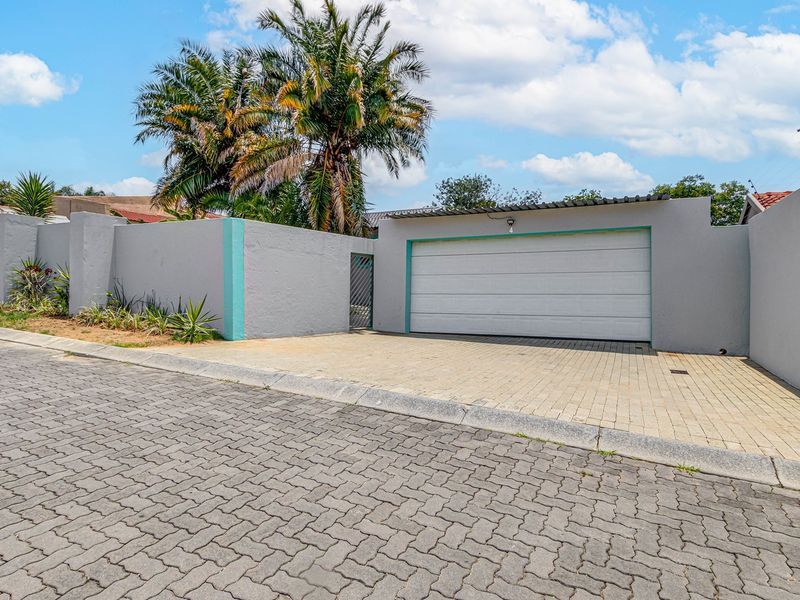 Front view of the property featuring a paved driveway, secure garage door, and perimeter wall with integrated electric fencing.