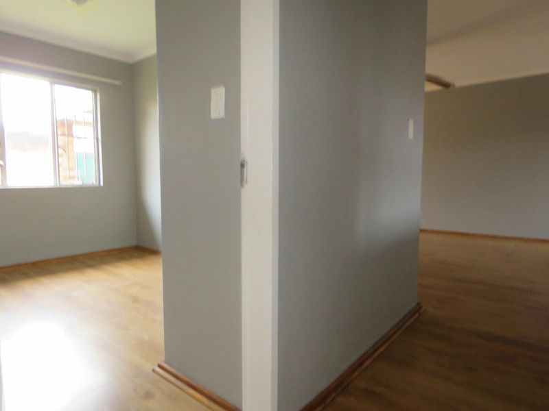 An empty, open-plan living area featuring neutral grey walls, laminate flooring, and natural light from a sliding window.