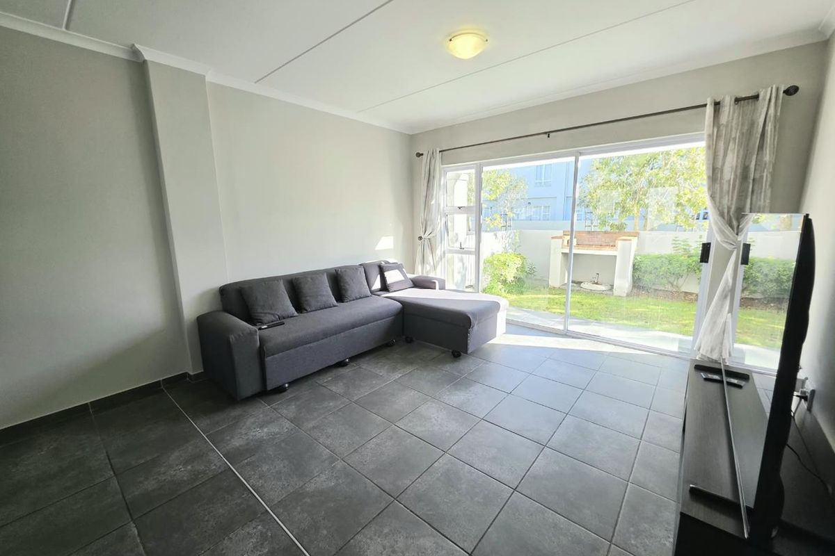 A bright living room featuring large format floor tiles and a sliding glass door providing direct access to the rear garden and patio area.