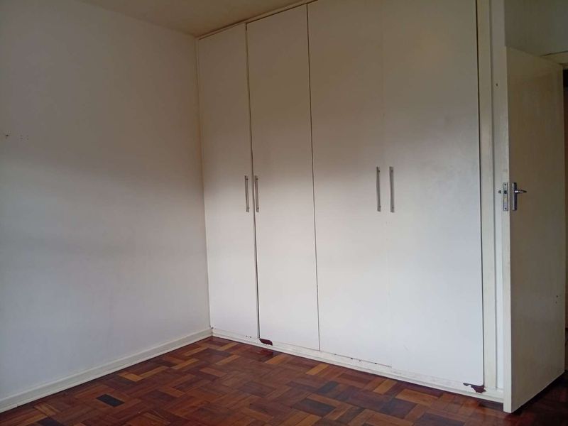 A vacant bedroom featuring classic parquet flooring and floor-to-ceiling built-in cupboards with modern handles.