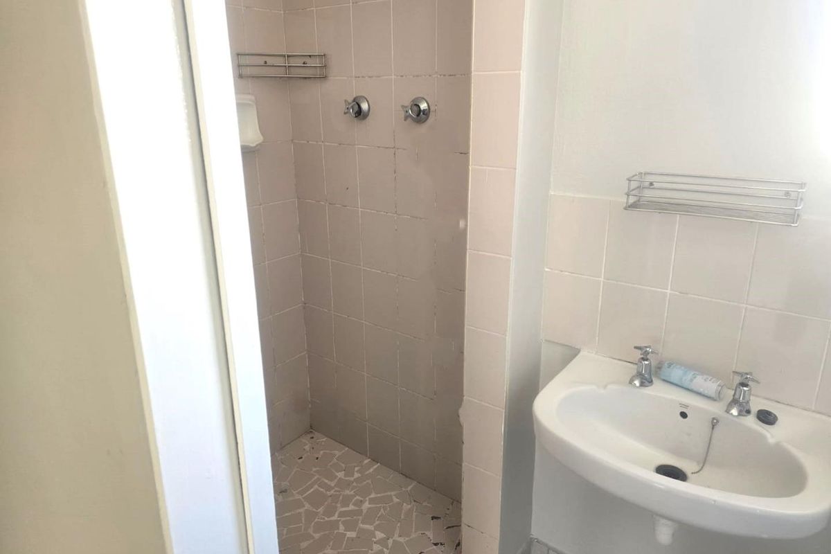 A dated bathroom featuring a tiled shower enclosure and a wall-mounted basin with chrome fixtures, requiring cosmetic updates to modernize the space.
